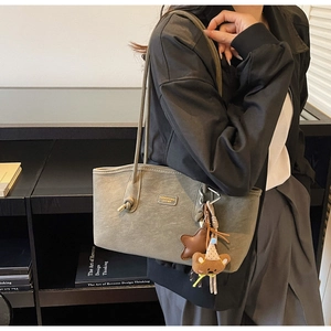Détail du sac cabas en cuir gris avec un pendentif ours mignon et une longue bandoulière