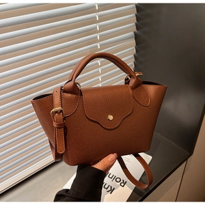 Detail view of brown lychee grain leather handbag with stylish wavy flap and gold button