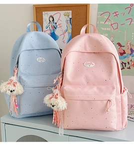 Polka dot backpacks in blue and pink with cute plush dog pendants on a wooden desk