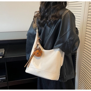 Detail of white leather hobo bag with cute brown bear charm on black leather jacket