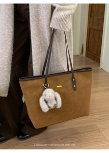 Detail of brown matte tote bag with slim shoulder straps and white plush rabbit charm