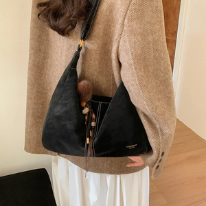 Close-up of black leather hobo bag with tassel pendant worn by model in a blazer