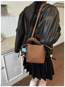 Détail d'un sac seau en cuir marron avec poignée tressée et charm ourson en peluche