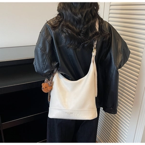 Close-up of white leather tote bag featuring a plush bear charm on a black jacket