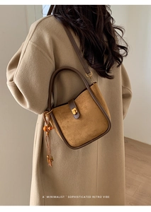 Sac seau en daim marron avec breloque en perles de bois porté par un mannequin en manteau beige