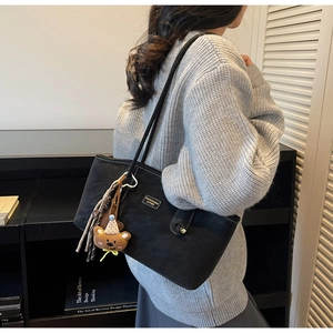 Détail du sac cabas en cuir noir avec breloque ours et pompon tissé sur la bandoulière