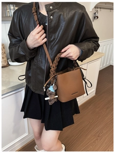 Detail of brown leather bucket bag with ring handle and a cute teddy bear charm