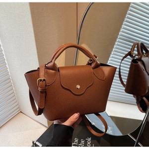 Detail of brown lychee grain leather handbag featuring metal buckle and mirror reflection