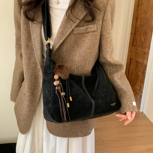 Detail of black suede hobo bag featuring white contrast stitching and tassel charm