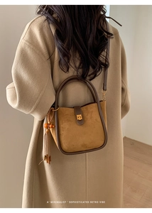 Détail du sac seau rétro en daim avec anses rondes, fermoir doré et gland à perles