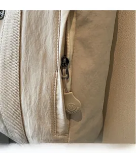 Close-up of beige nylon tote bag with textured fabric and branded plastic zipper pull