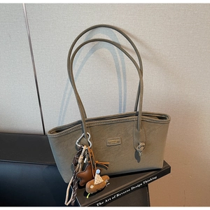 Détail du sac cabas vert olive avec breloque ours et boucle coeur sur un livre design