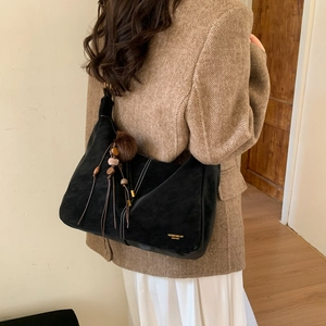 Detail of black suede hobo bag with contrast stitching and teddy bear pendant accessory