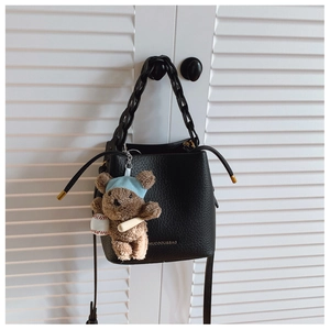 Detail of black pebble leather bucket bag with chain strap and teddy bear charm