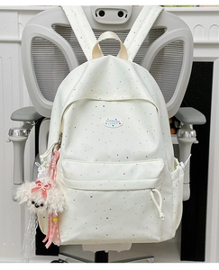 Close-up of beige polka dot backpack with plush dog keychain and logo patch detail