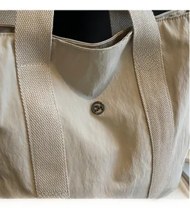 Macro detail of khaki nylon tote bag featuring CM metal logo and woven strap texture