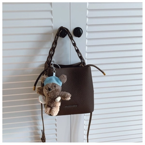 Detail view of deep brown pebbled leather bucket bag with chunky chain and bear charm