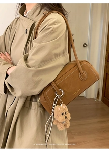 Close-up of caramel suede crossbody bag with bear pendant and white stitching details