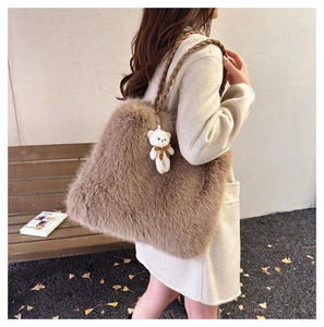 Detail of a large brown faux fur tote bag with a cute bear pendant on a woven strap