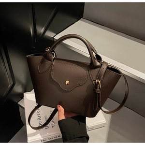 Detail of dark brown lychee leather handbag with golden buckle and wavy edge flap