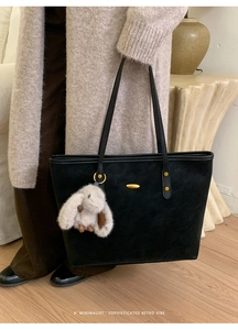 Detail of black suede tote bag featuring gold hardware and a cute rabbit charm accessory