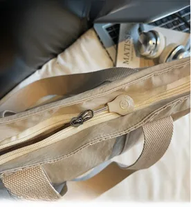 Detailed close-up of metal zipper and rubber M-logo puller on khaki nylon tote bag