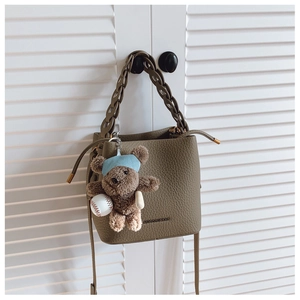 Detail of olive green lychee grain leather bucket bag with cute bear charm and woven handle