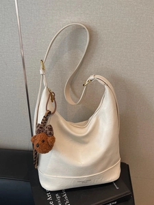 Creamy white hobo shoulder bag with a cute bear pendant on a grey background