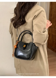 Modèle portant un sac seau en cuir verni noir avec fermoir doré et gland en perles