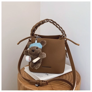 Detail of brown pebbled leather bucket bag with woven handle and cute bear charm pendant
