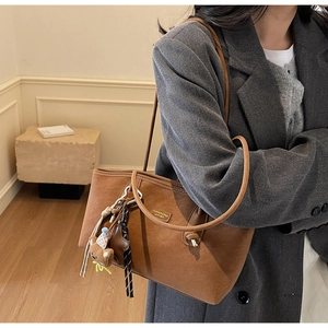 Détail du cabas en daim marron avec breloque ours porté par un mannequin en blazer gris