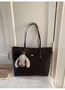 Detail of dark brown tote bag with gold metal ornament and plush rabbit keychain