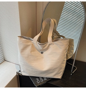 Detail of off-white nylon tote bag with round buckle on a black display stand