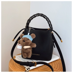 Detail of black lychee grain bucket bag featuring a woven handle and teddy bear charm