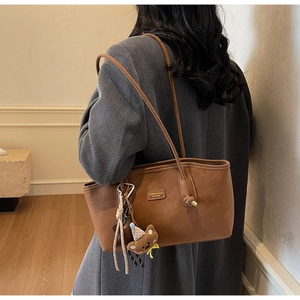 Sac cabas en daim marron porté par un mannequin en manteau de laine avec breloque