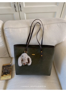 Detail of olive green tote bag featuring golden rivets and a plush bunny charm on a sofa