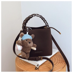 Detail of dark brown leather bucket bag with woven handle and baseball bear charm