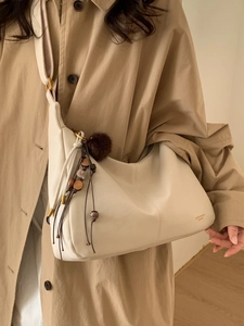 Chic cream leather hobo bag with decorative tassels and wood beads worn on a shoulder