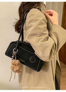 Detail of black vintage underarm bag with white stitching and cute brown plush bear charm