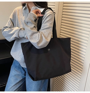 Close-up of black nylon tote bag with circular metal CM logo worn with casual outfit