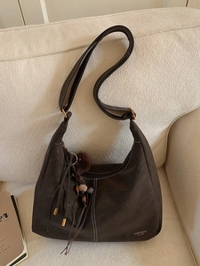 Deep brown retro leather hobo bag with contrast stitching and tassel charm on a sofa