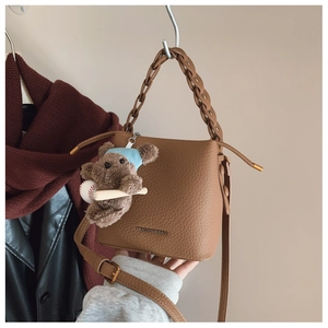 Brown bucket bag featuring woven handle and cute teddy bear charm with striped hat