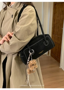 Detail of black suede crossbody bag with white stitching and a cute teddy bear charm