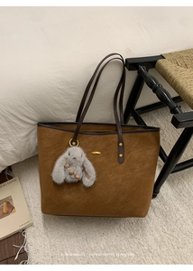 Detail of brown suede tote bag with leather handles and cute bunny keychain accessory