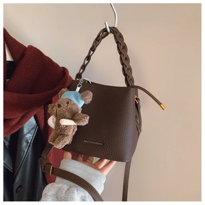 Macro shot of dark brown pebbled leather bucket bag with chain strap and bear charm