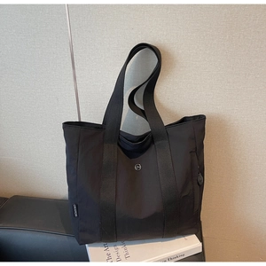 Close-up of black nylon tote bag with round metal logo and vertical side zipper detail