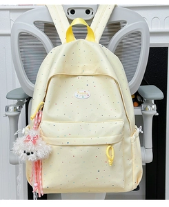 Detail view of light yellow polka dot backpack with a cute white plush dog charm