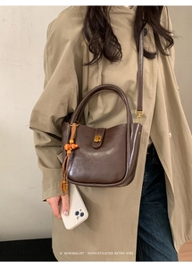 Détail du sac seau marron vintage avec garniture dorée et pompon bohème sur trench-coat