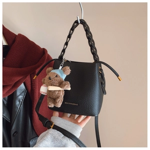 Detail of black lychee grain leather bucket bag with woven chain and cute bear charm