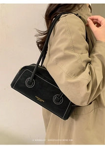 Close-up of black suede shoulder bag with white contrast stitching and gold lettering